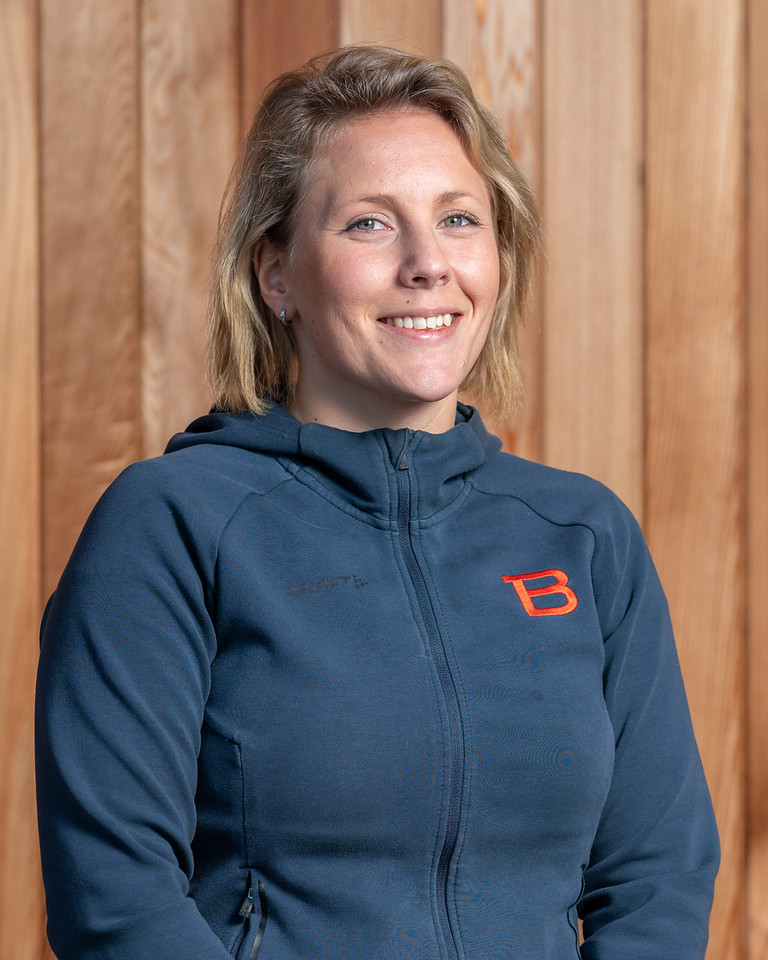 En kvinna i en blå Bergstrands hoodie som står framför en trävägg.
