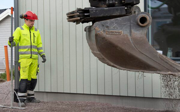 En byggnadsarbetare står bredvid en stor grävmaskin.