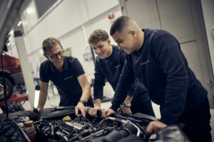 Tre män som arbetar på en bilmotor i ett garage.