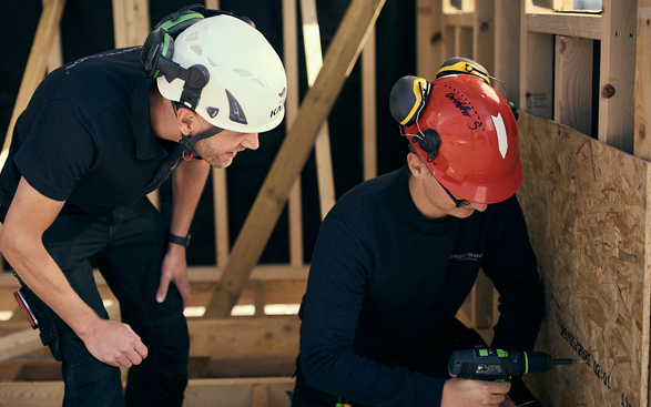 Elev_larare-587×367 Två män som arbetar på en träkonstruktion.