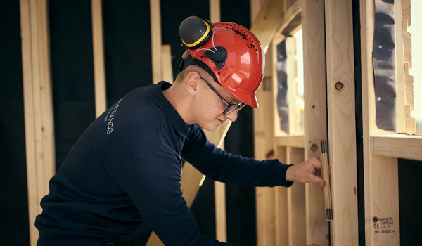 husbyggnad_600x350 En man i en röd hatt arbetar på en vägg.