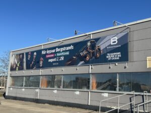 ny skylt märsta En stor banner på en grå byggnad annonserar öppnandet av Bergstrands med bilder på arbetare och byggutrustning samt information om öppningsdatum i augusti 2025.